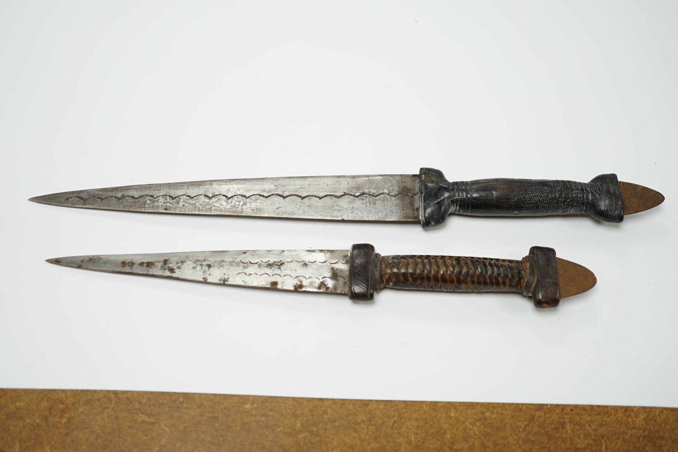 Two African Tuareg arm daggers, with leather grips and leather sheaths, longest blade 20cm. Condition - good